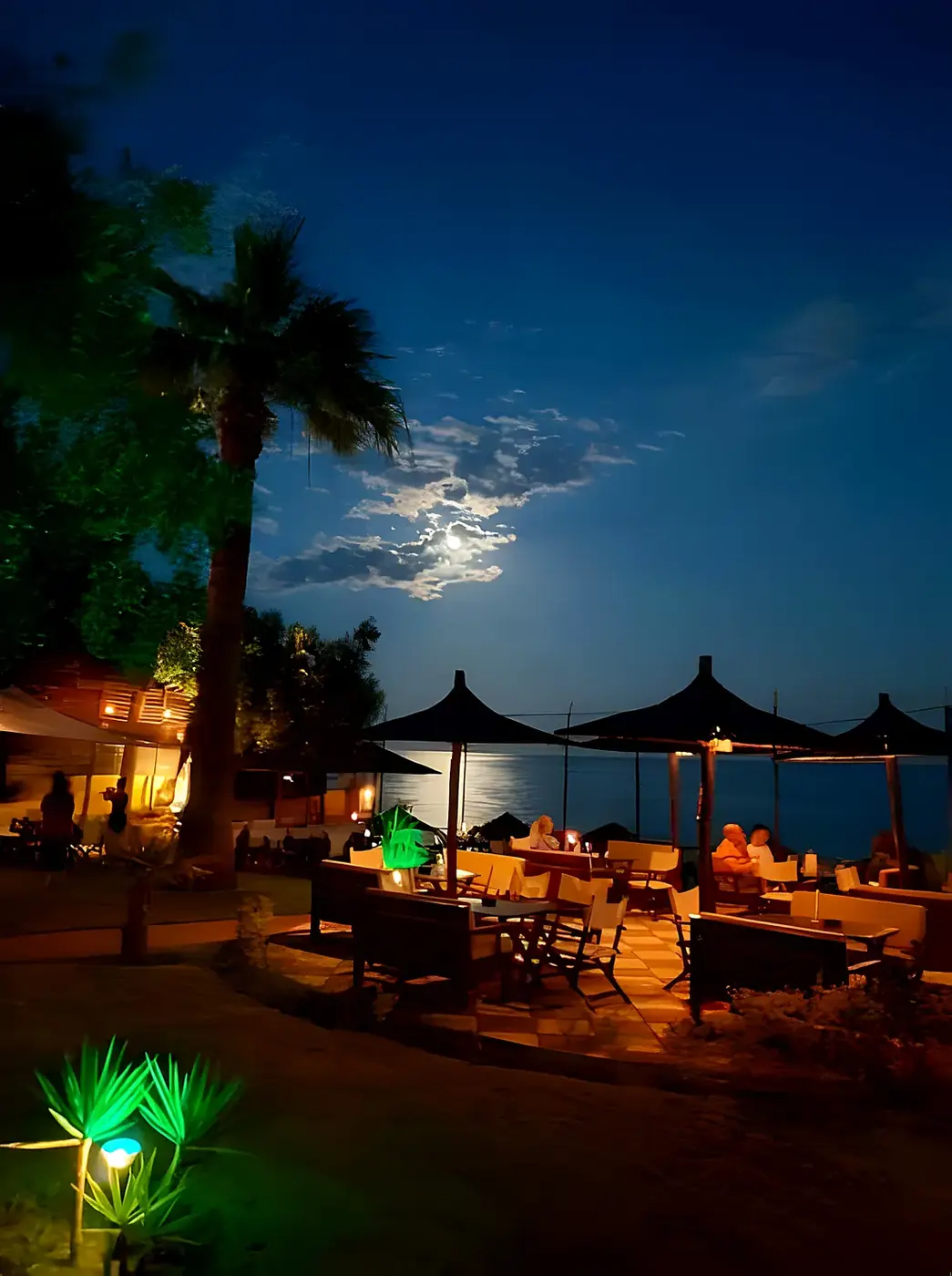 Kudu's terrace after dark, lanterns and garden lights glowing over the night sea