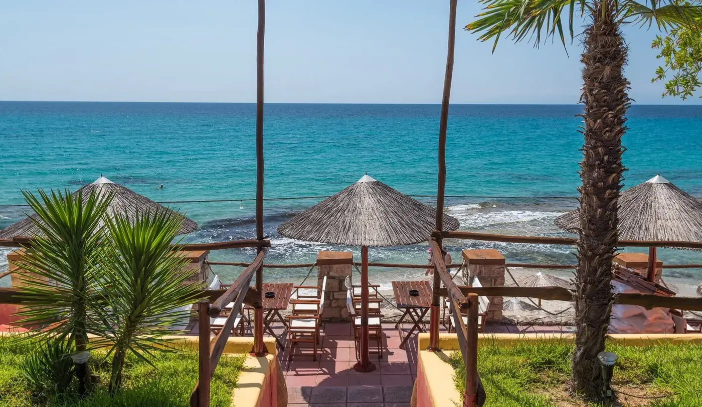 Straw umbrellas on Kudu's terrace above turquoise Aegean water